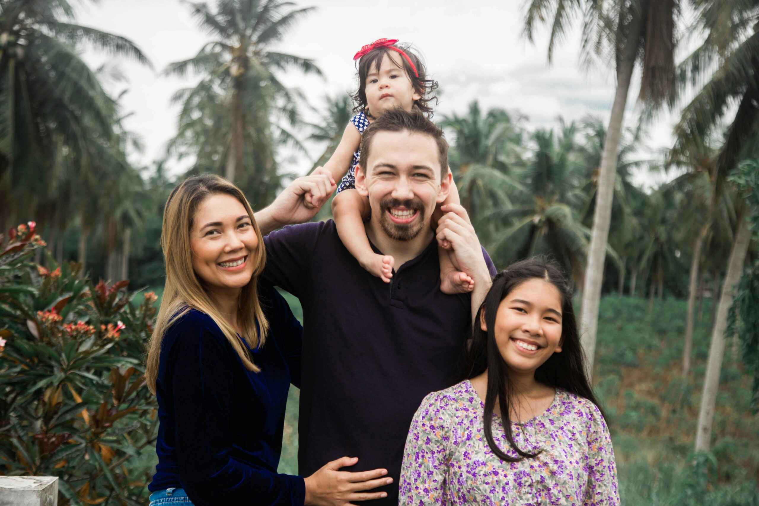 A joyful family enjoys time together outdoors with palm trees in the background.